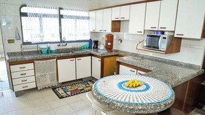 A kitchen with white cabinets, a granite countertop, a microwave, and a table with a crocheted tablecloth. - CHÁCARA BELLA VITTA <br>WANT COMFORT, PEACE, SECURITY. A HEATED POOL. HE COMES. (socorro)