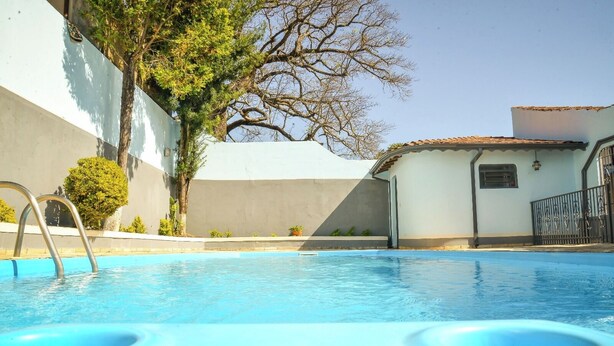 A swimming pool with a metal ladder, surrounded by a building with a tiled roof and a tree. - CHÁCARA BELLA VITTA <br>WANT COMFORT, PEACE, SECURITY. A HEATED POOL. HE COMES. (socorro)