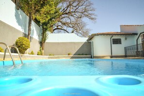 A swimming pool with a metal ladder, surrounded by a building with a tiled roof and a tree.