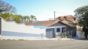 A residential street with a white wall, a garage, and a house with a tiled roof. - CHÁCARA BELLA VITTA <br>WANT COMFORT, PEACE, SECURITY. A HEATED POOL. HE COMES. (socorro)