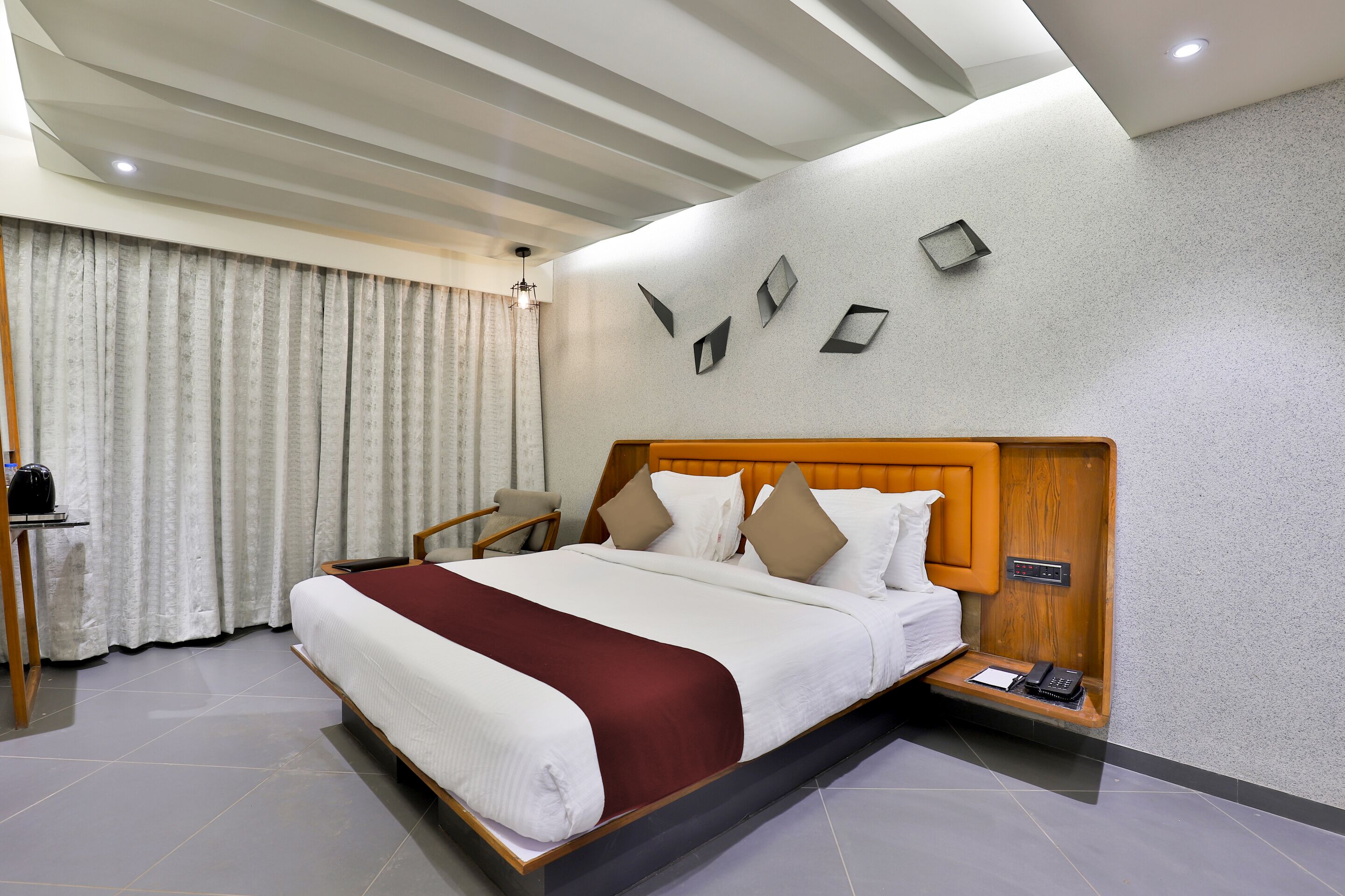 Una habitación de hotel moderna con una cama grande, cabecero de madera, un escritorio con una silla y una mesita de noche con una lámpara.