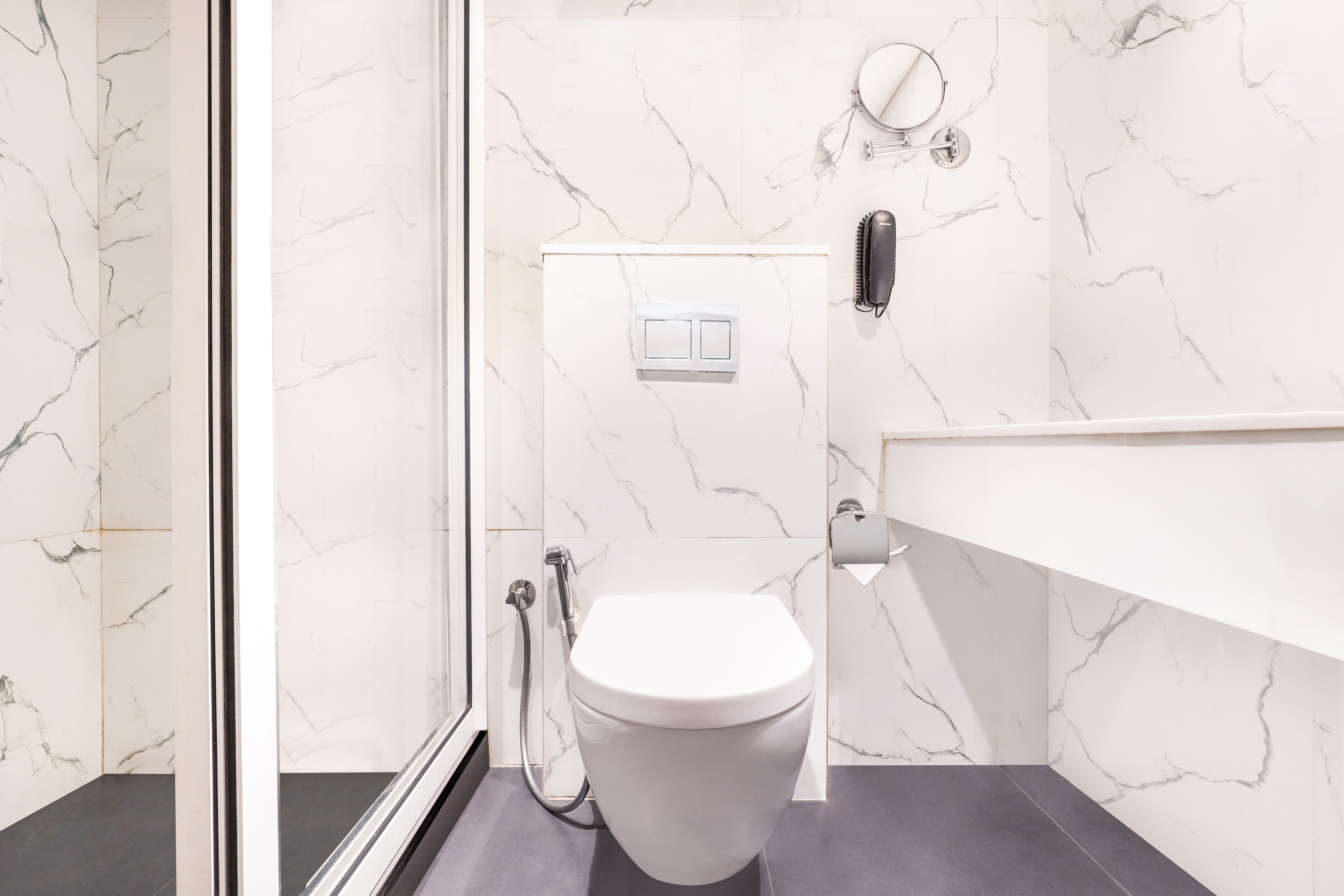 Une salle de bain moderne avec des toilettes blanches, des murs en marbre et un sol foncé.