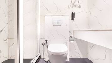 Une salle de bain moderne avec des toilettes blanches, des murs en marbre et un sol foncé.