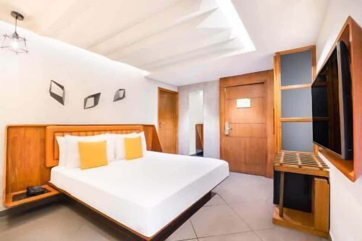 A hotel room with a bed, a TV, and a wooden headboard.