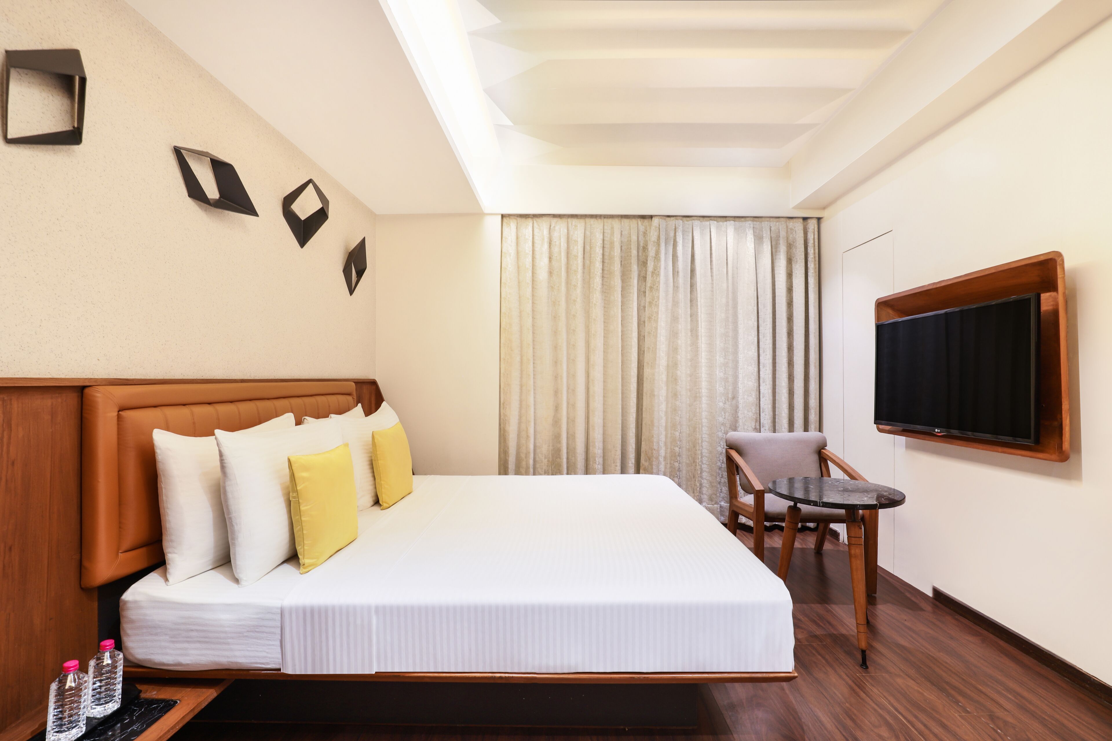 A hotel room with a large bed, a small table, a chair, a TV, and a window with curtains.