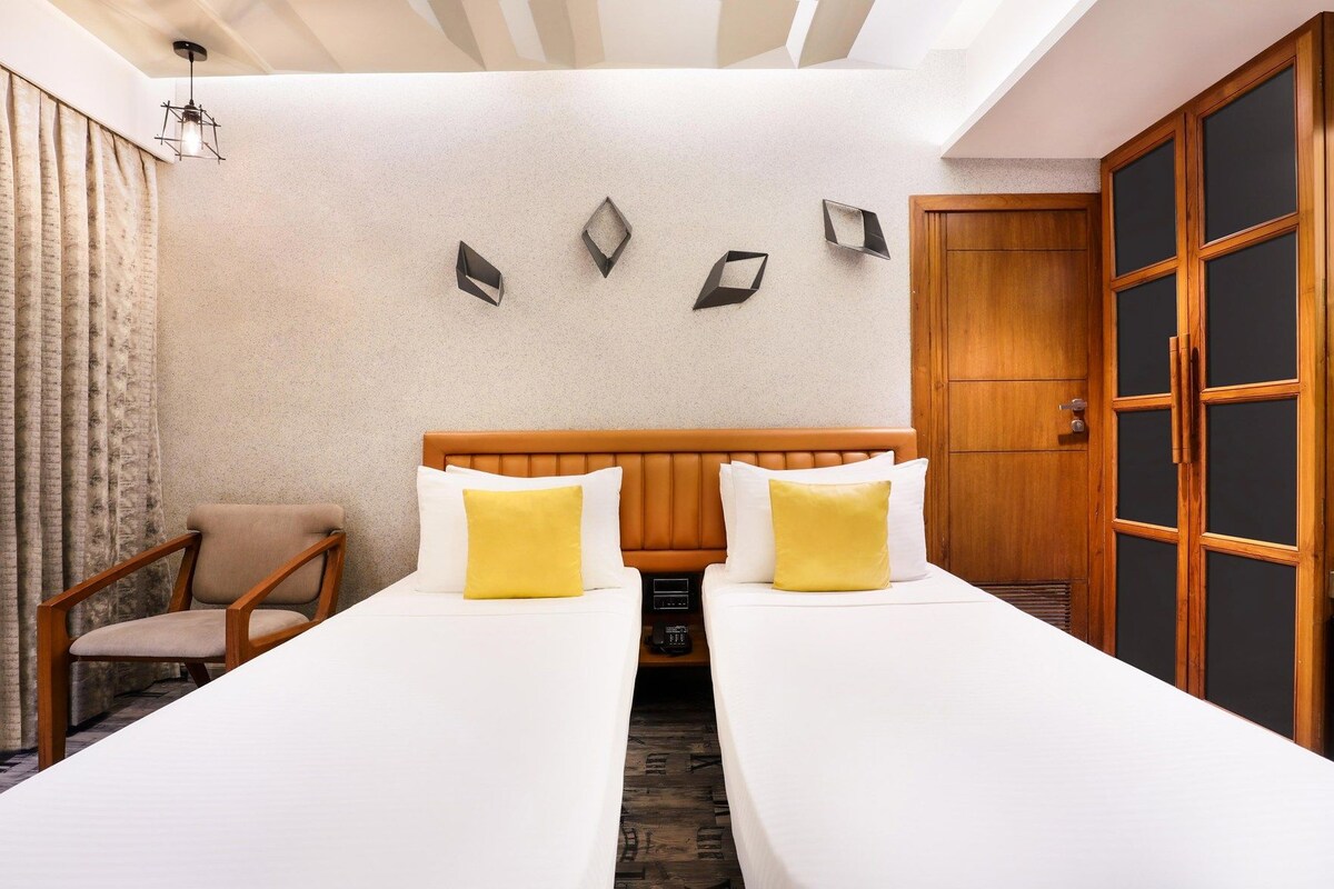 Une chambre d’hôtel avec deux lits, une armoire en bois, une chaise et un luminaire fixé au mur.