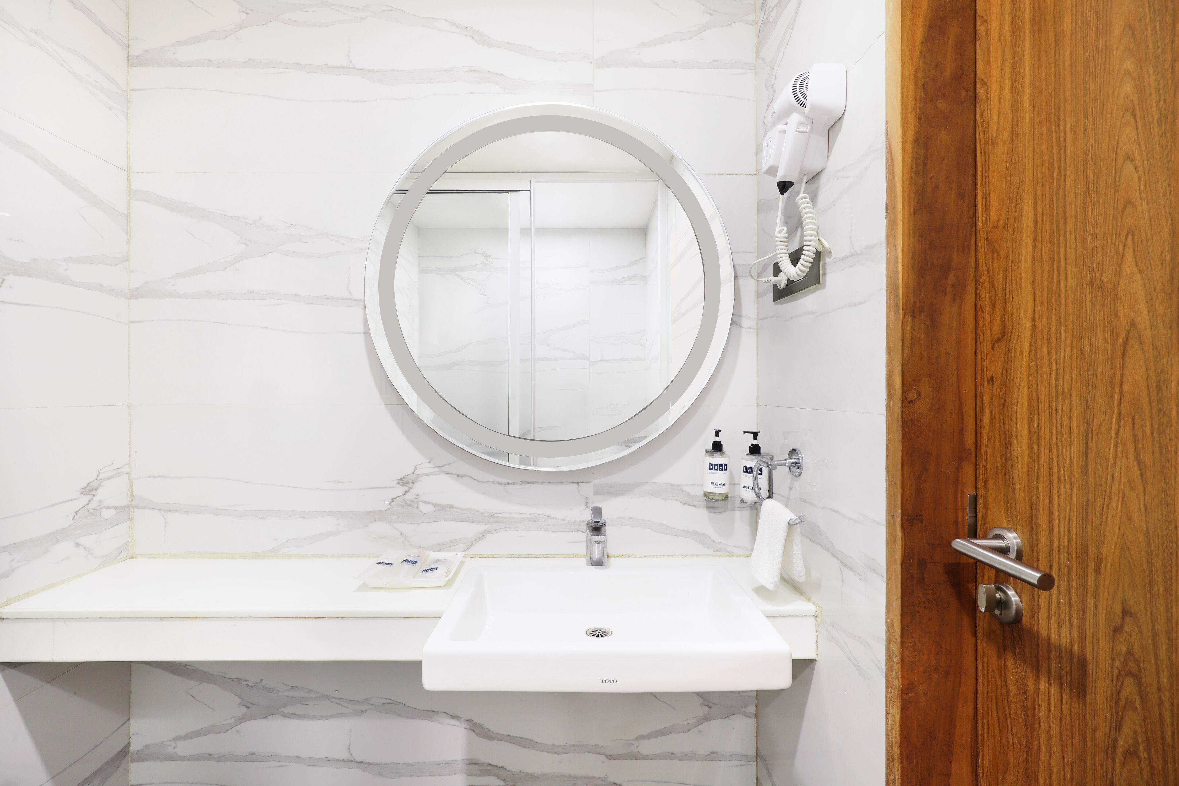 Une salle de bain avec un lavabo blanc, un miroir rond, un sèche-cheveux et des articles de toilette posés sur le comptoir.