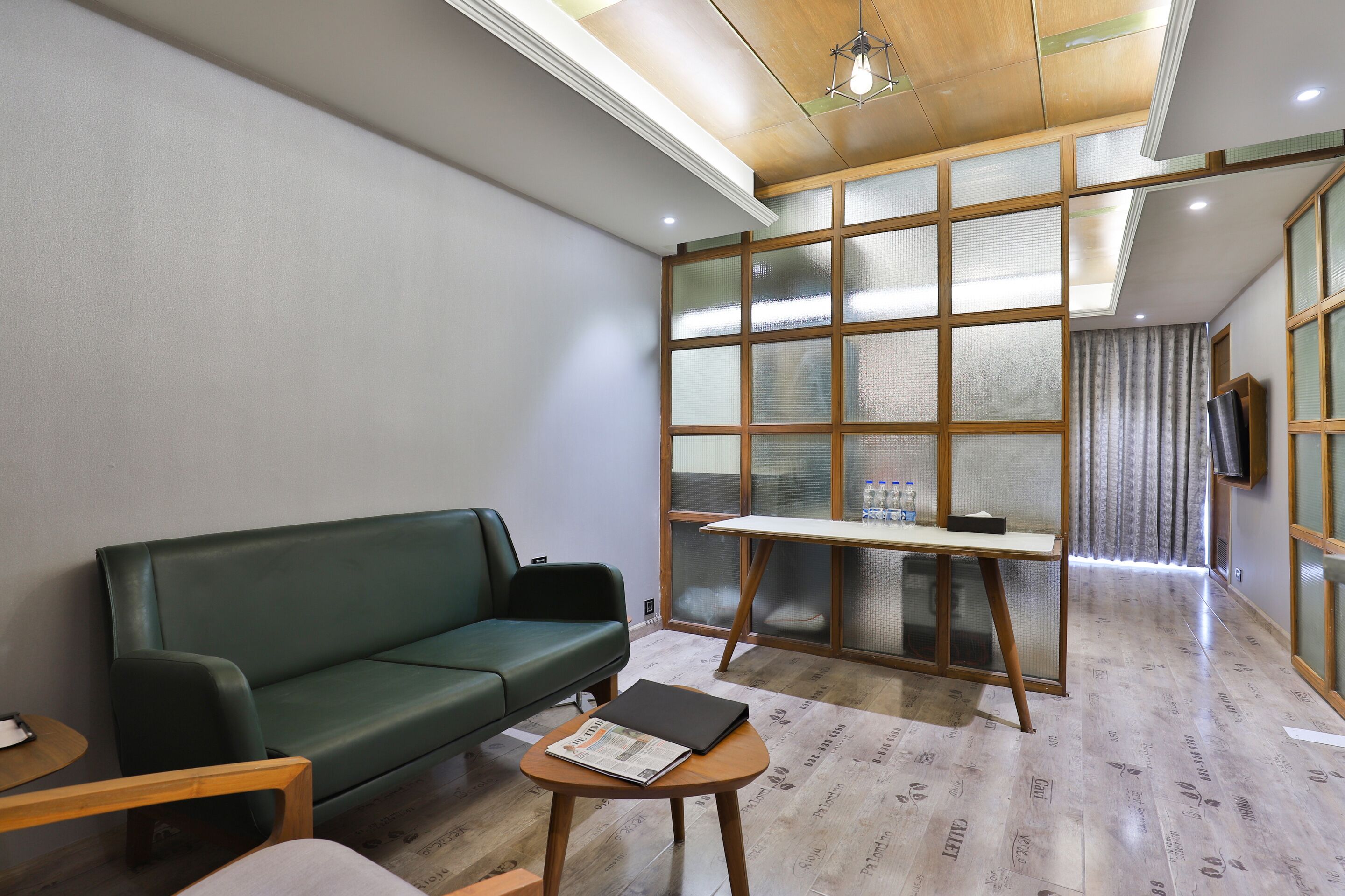 A modern room with a green sofa, a small wooden table, and a partition with frosted glass panels.