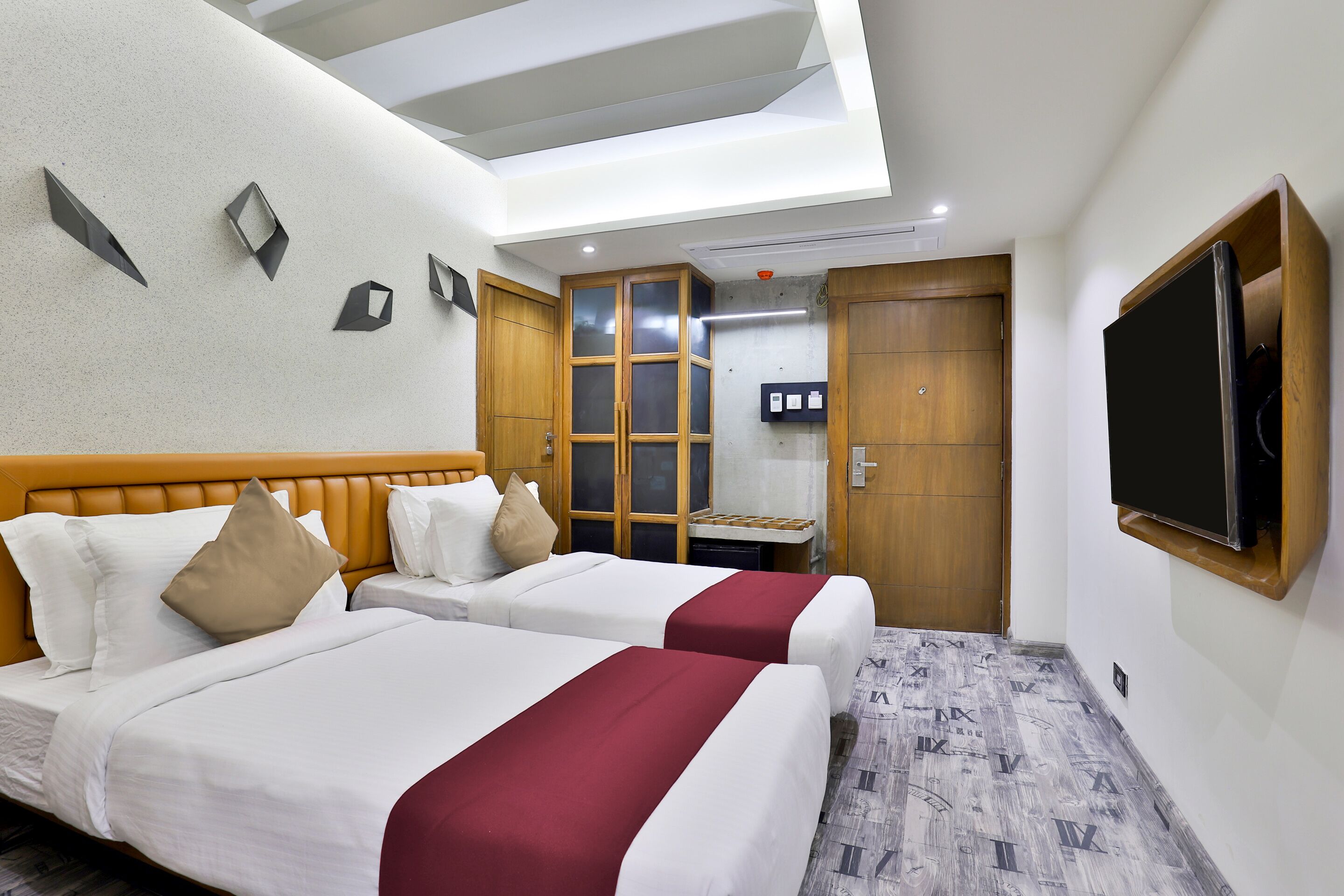 A hotel room with two beds, a TV, a wardrobe, and a ceiling light.