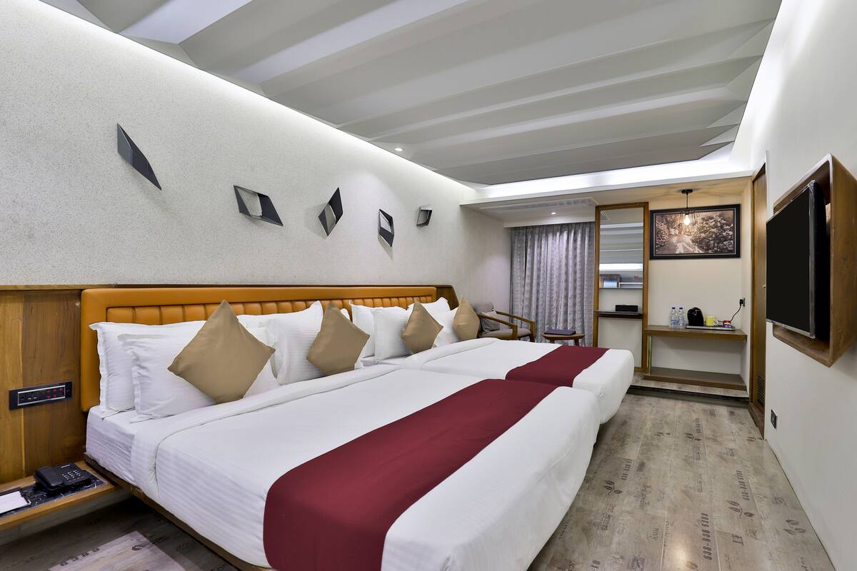 A hotel room with a large bed, a wooden headboard, a flat-screen TV, a desk, and a window with curtains.