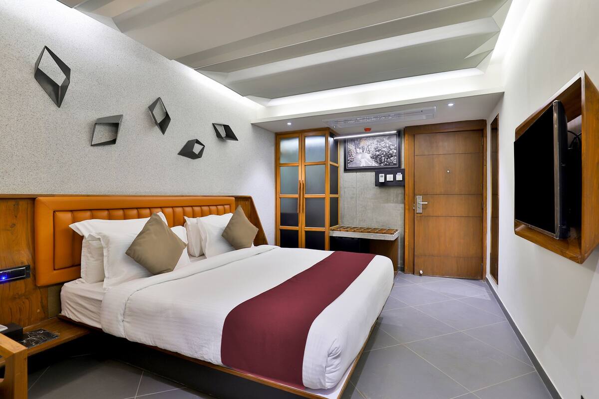A modern hotel room with a large bed, a wooden headboard, a TV mounted on the wall, and a small table with a chair.