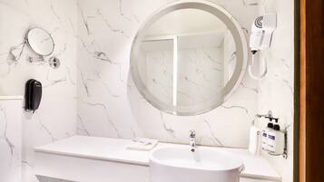 A bathroom with a white marble wall, a round mirror, a white sink, a hairdryer, and a telephone.