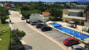 A parking area with a swimming pool, a covered seating area, and a view of a residential area with houses and greenery. - Condo  Blanca!!!!!!! (Nuevo Vallarta)