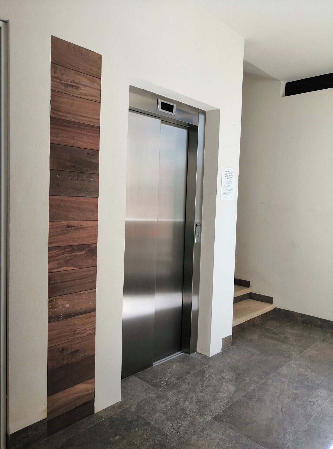 An elevator with a metallic finish, adjacent to a wall with a wooden panel design.