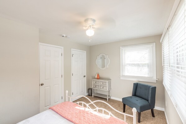 A bedroom with a bed, a dresser, a chair, and a window with blinds.