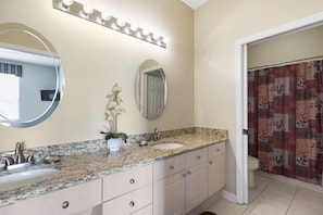 A bathroom with a granite countertop, two sinks, a mirror, and a shower curtain.