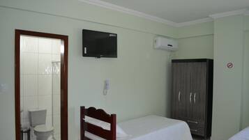 Un dormitorio con cama, armario, televisor y baño con inodoro y cubo de basura.