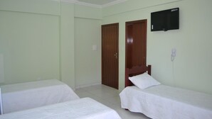 Une chambre avec deux lits simples, un téléviseur fixé au mur et une porte en bois.