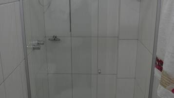 Een kleine, afgesloten douchecel met een toilet en een geel plankje erboven.