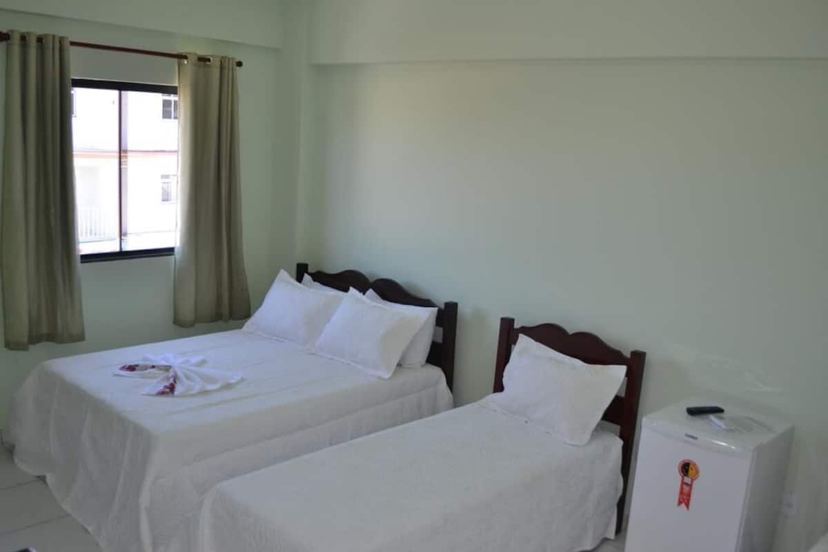 Ein Hotelzimmer mit zwei Einzelbetten, einem Fenster mit Vorhängen, einem Nachttisch und einem kleinen Kühlschrank.