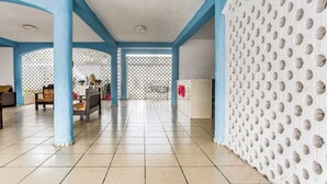 A spacious indoor area with tiled flooring, blue structural columns, and a white wall with circular patterns. - OYO Hotel Jaguar (Cancun)