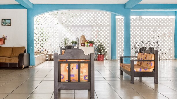 A spacious room with two wooden chairs, a sofa, and a decorative wall with circular cutouts. - OYO Hotel Jaguar (Cancun)