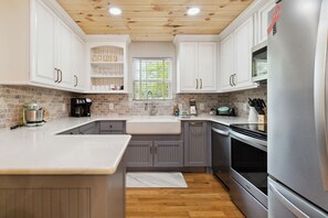 A modern kitchen with white cabinets, a built-in oven, and a stainless steel refrigerator. - Welcome to “Relax Inn” Retreat at Lake Cumberland – A Perfect Cabin Escape (Burnside)
