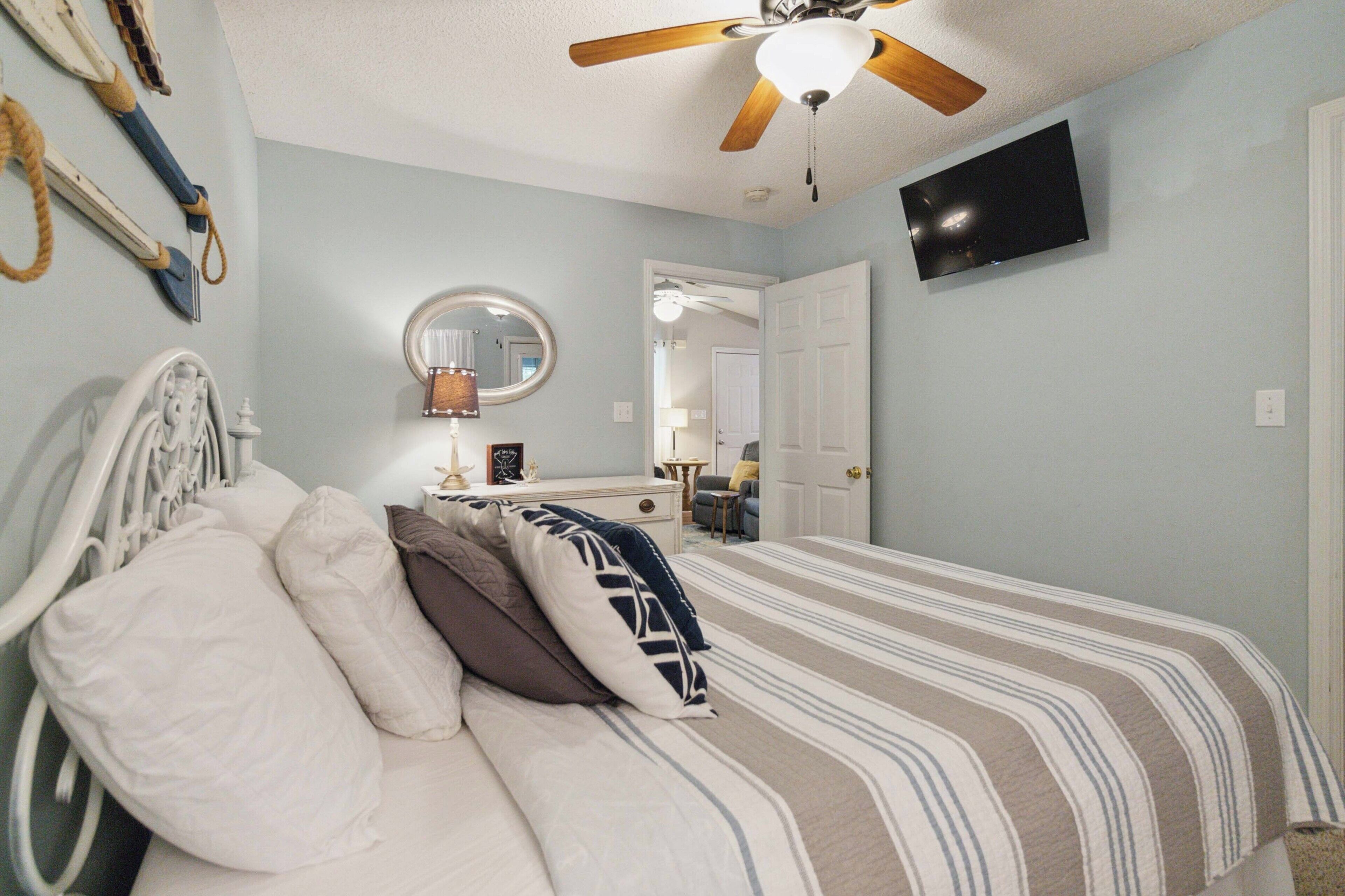 A bedroom with a bed, a ceiling fan, a TV, and a door leading to another room.