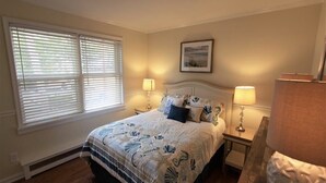 A bedroom with a large bed, two bedside tables with lamps, a framed picture on the wall, and a window with blinds. - Pet friendly cottage by the Delaware Bay-Townbank  (Townbank)