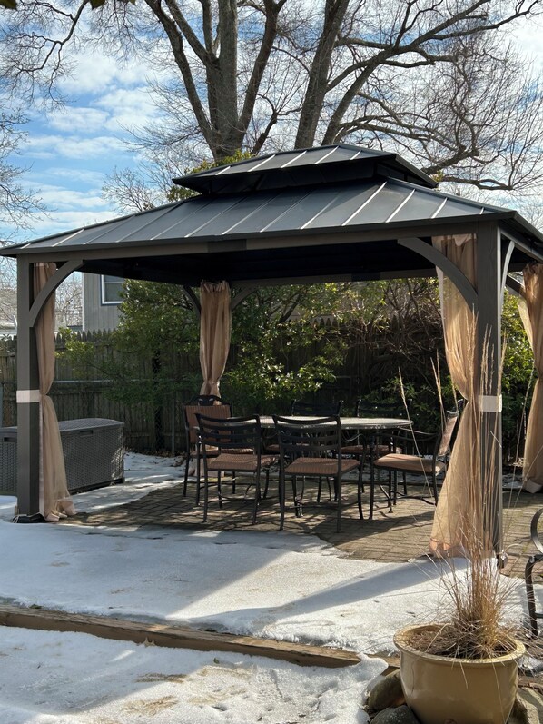 A gazebo with a table and chairs, surrounded by snow and trees.