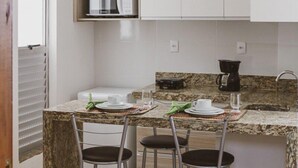 Una cocina compacta con armarios blancos, microondas, cafetera y encimera de granito.