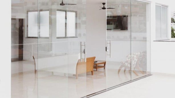 Un interior moderno con un separador de vidrio, un ventilador de techo y una silla de madera.