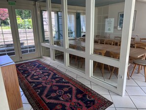 A room with a patterned rug, a wooden cabinet, and a dining area with tables and chairs. - Group house for up to 30 people in the Southern Harz Mountains - Group house for up to 30 people (Bad Sachsa)