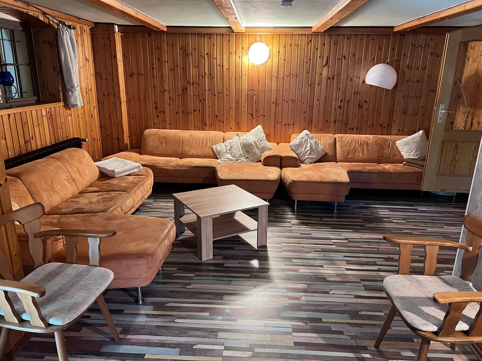 A cozy room with a wooden wall, a brown sofa set, a wooden coffee table, and a patterned floor.