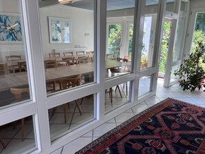 Een ruime eethoek met glazen wanden, houten tafels en stoelen.