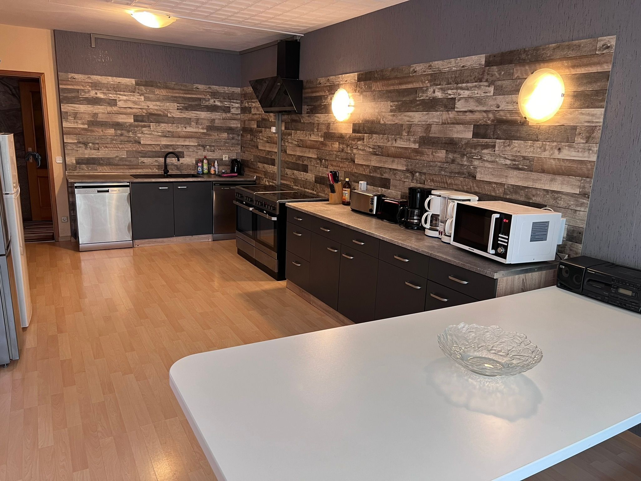 A modern kitchen with a white countertop, stainless steel appliances, and wooden wall accents.