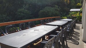 Un espace extérieur aménagé pour les repas, avec plusieurs tables et chaises, entouré de verdure.