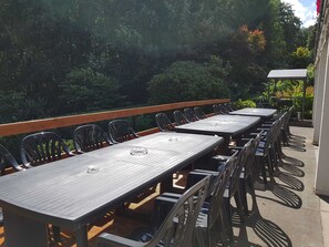 Een terras met meerdere tafels en stoelen, omringd door groen.