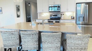 Una cocina moderna con una isla central, electrodomésticos de acero inoxidable y sillas de mimbre.