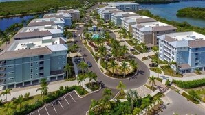Un hotel frente al mar con varias edificaciones, una piscina central y un puerto deportivo.