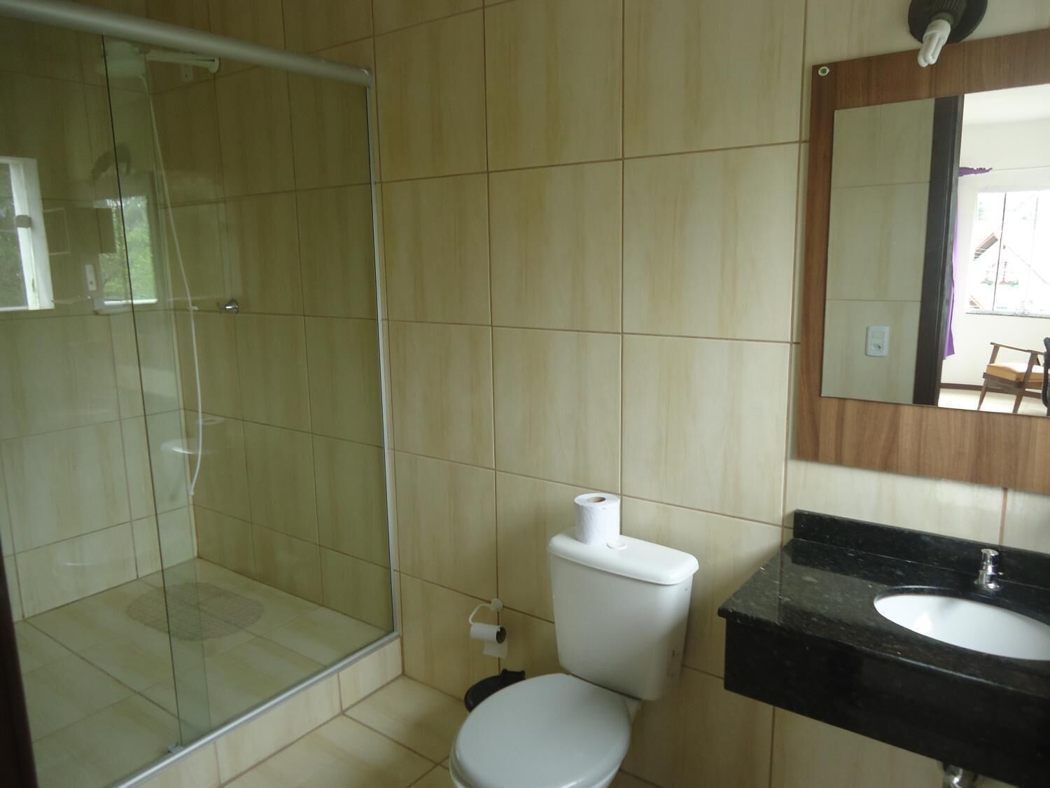Casa de banho com chuveiro de cabine de vidro, sanita e lavatório com espelho em cima.