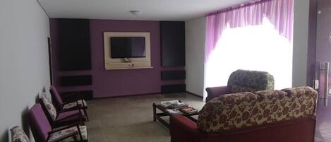 Una sala de estar con un sofá, sillones, una mesa de centro y un televisor de pantalla plana montado en la pared.