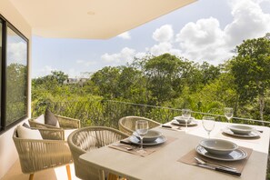 A dining area with wicker chairs and a table set for two, overlooking a lush green landscape. - Neem Tulum (Tulum)
