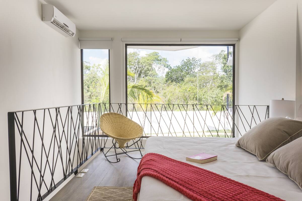 Un dormitorio con un ventanal grande, una cama, una silla y vistas a la vegetación.