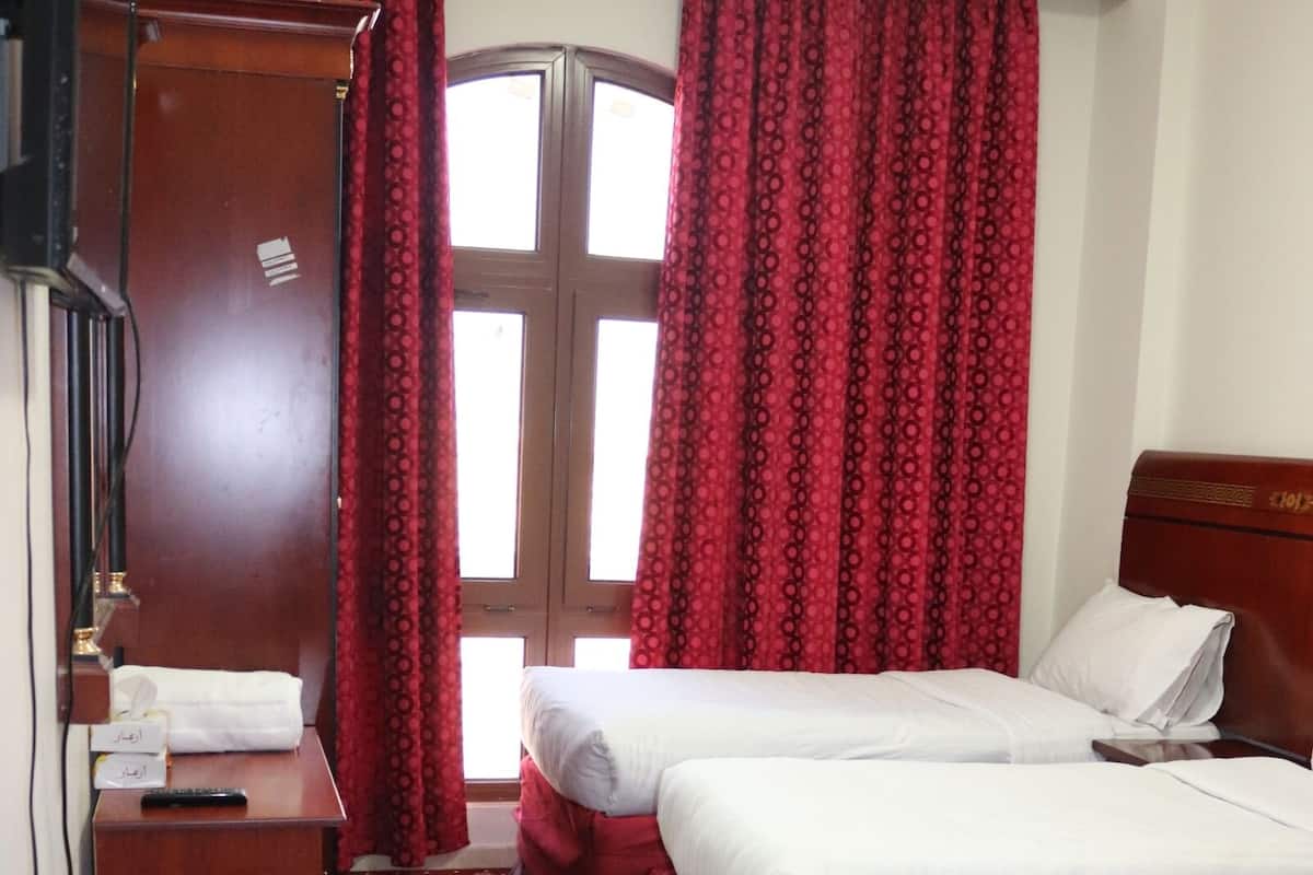 Une chambre d’hôtel avec deux lits, un bureau en bois, une armoire et une grande fenêtre avec des rideaux rouges.