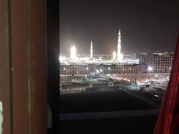 A view of a mosque with two minarets and a large central dome, surrounded by buildings and a parking area.