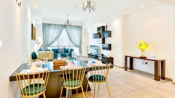 A modern dining area with a glass-top table, three wicker chairs, and a chandelier.