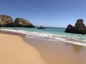 Una playa con agua turquesa cristalina, grandes formaciones rocosas y una orilla arenosa.