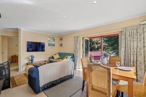 A bedroom with a bed, a TV, a dining area with a table and chairs, and a view of the outside.