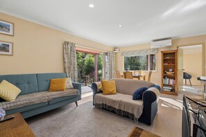 A living room with two sofas, a coffee table, a bookshelf, and a dining area with a table and chairs.